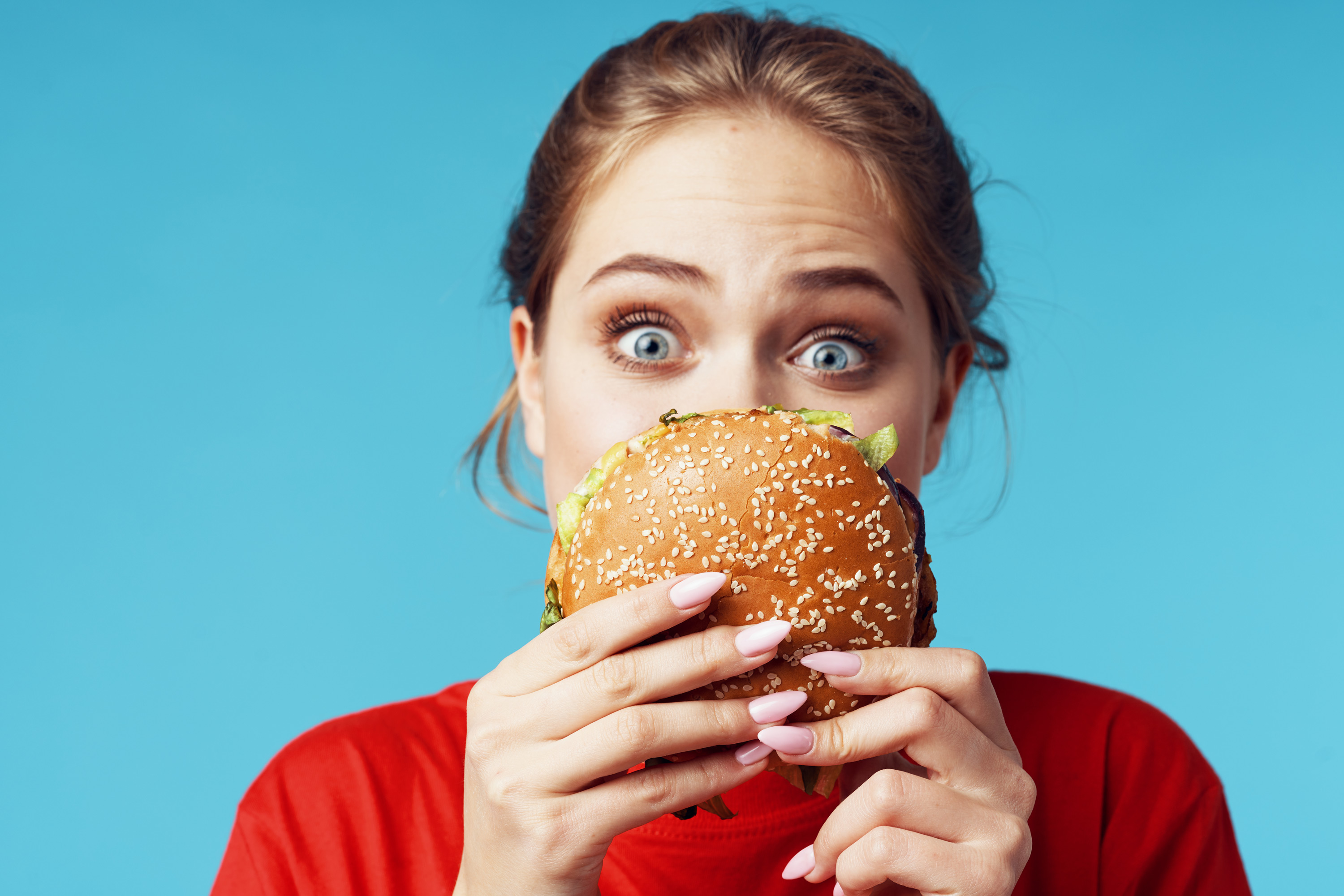 Women holding burger, looking quizzically at it. 