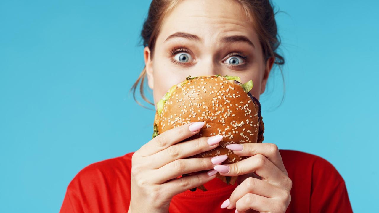 Women holding burger, looking quizzically at it. 