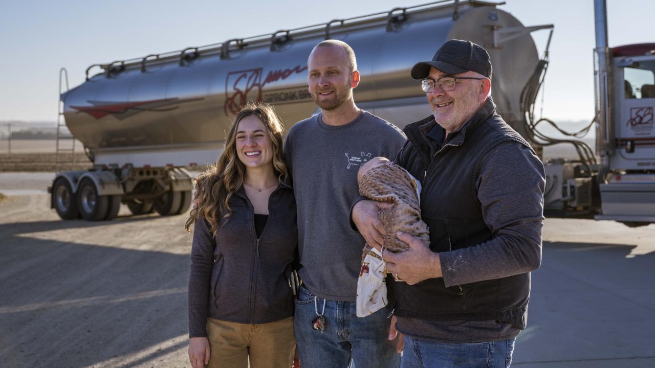 The Spronk family is standing alongside one another, smiling, as they stand in front of one of their farming trucks