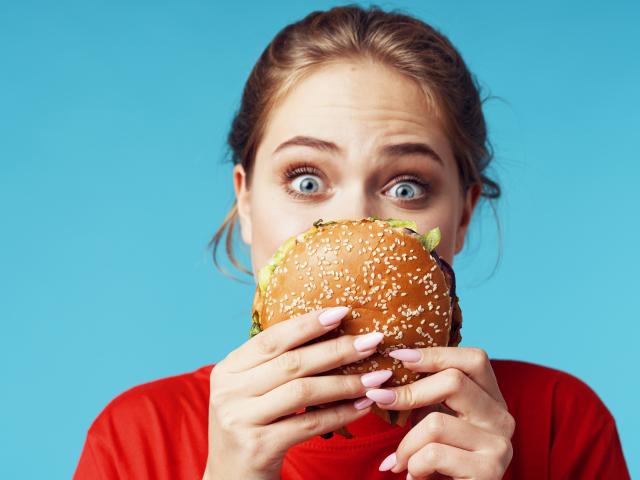 Women holding burger, looking quizzically at it. 
