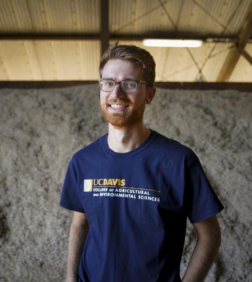 man with glasses standing in front of pile of cow feed and smiling
