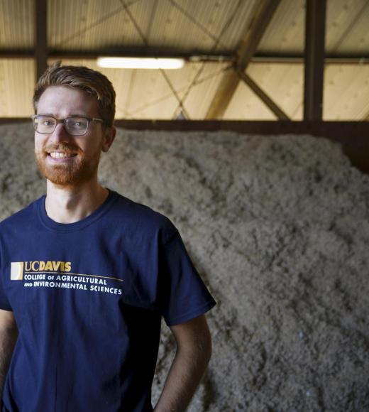 man with glasses standing in front of pile of cow feed and smiling