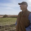 Dave Mensink is wearing a baseball cap and standing in his field looking outwards at it.