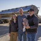 The Spronk family is standing alongside one another, smiling, as they stand in front of one of their farming trucks